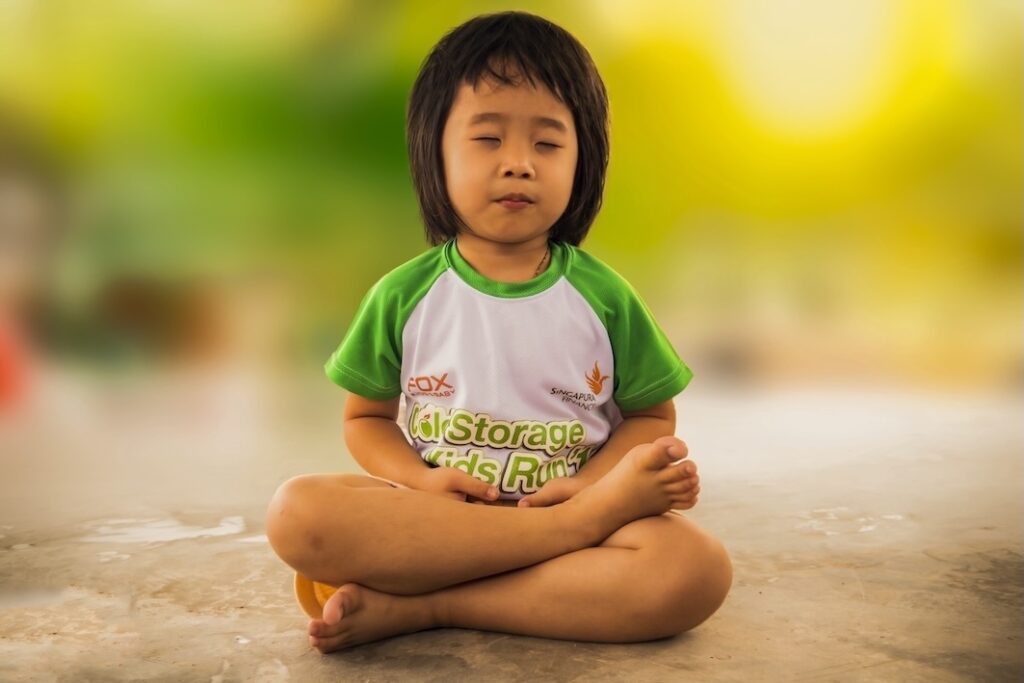 Young child sitting in half lotus position, meditating.